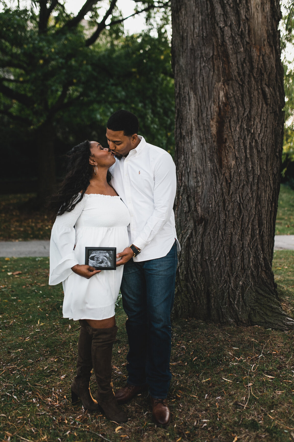 Maternity shot with soon to be mom, and dad kissing holding ultra sound photo.