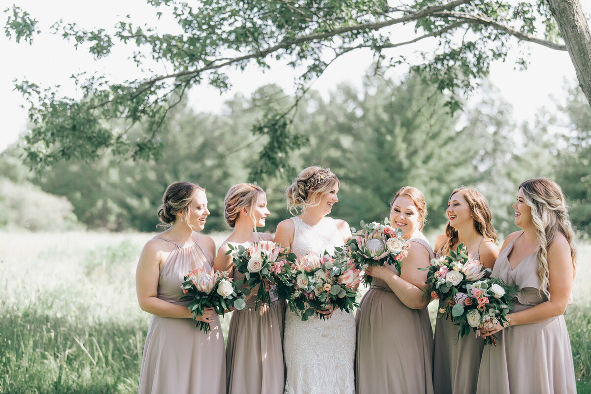 Bridesmaids wearing taupe dresses posing for traditional photos with the bride while all holding whimsical pink, ivory and green bouquets