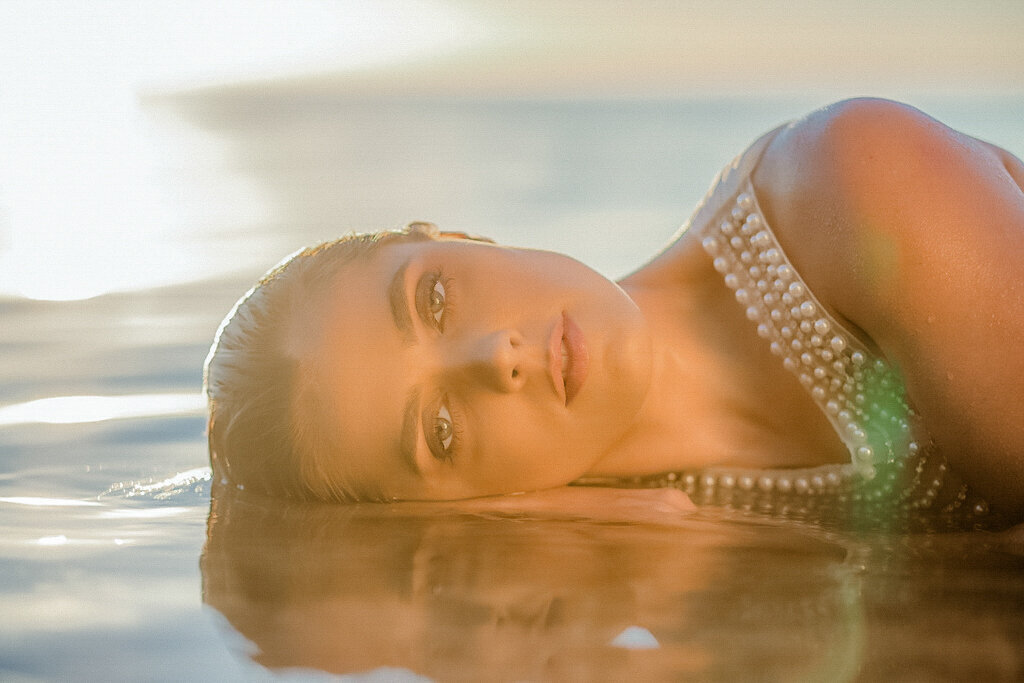 beautiful bride laying her head on ocean water in golden glow