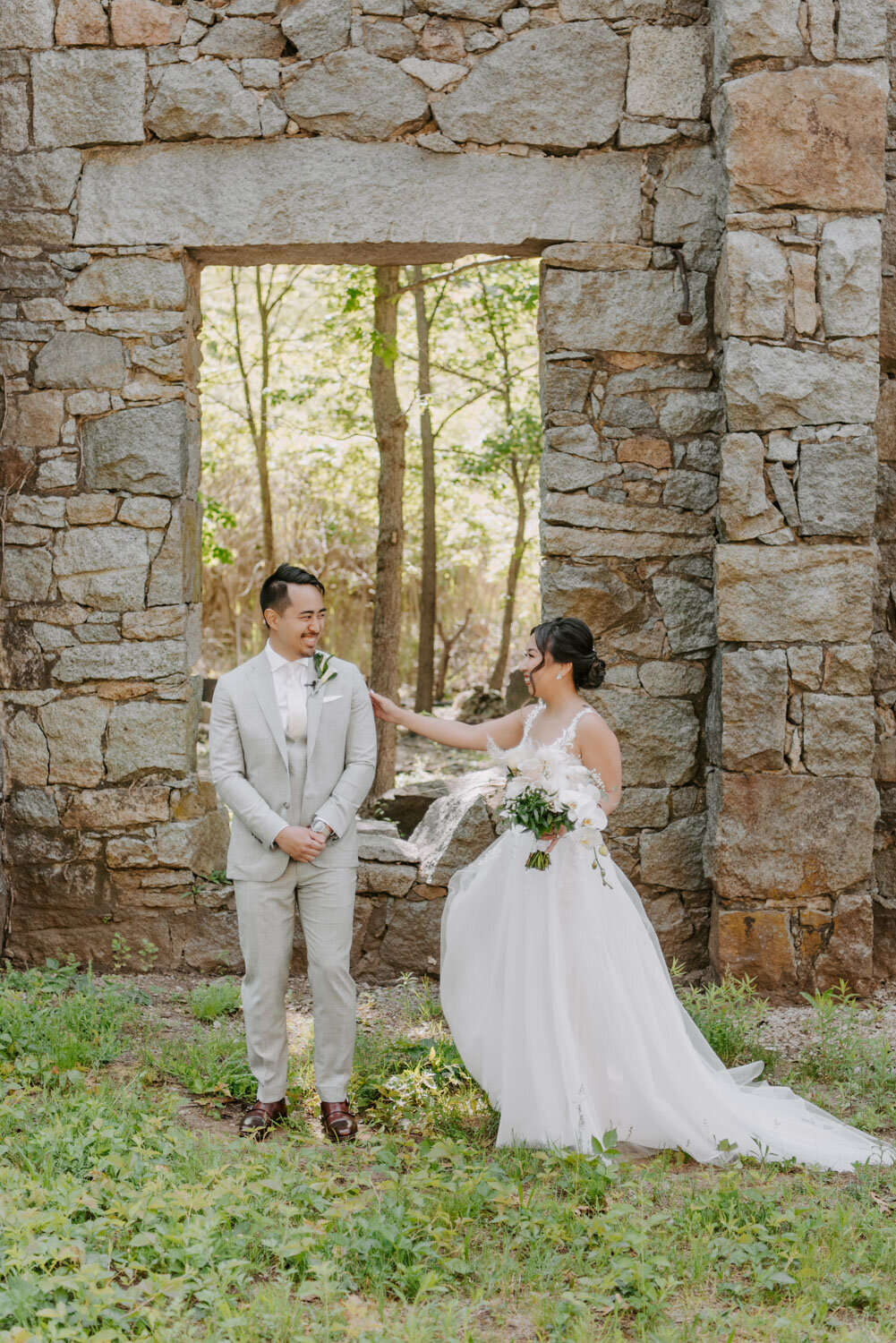 Bride tapping groom’s shoulder for a first look, surrounded by stone walls