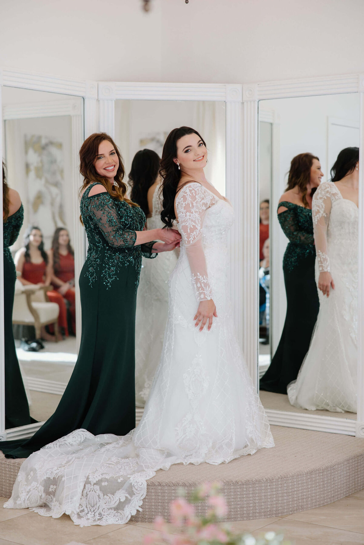 Mother of the bride in green sequin gown helping bride to get in to wedding dress on wedding day