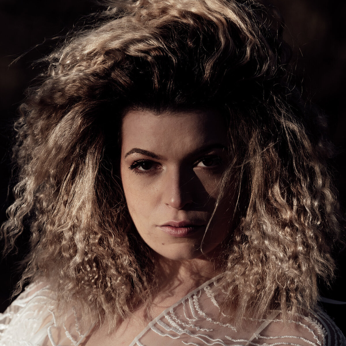 a boho bride in the autumn sun stares at the camera with incredible curly hair blowing in the wind