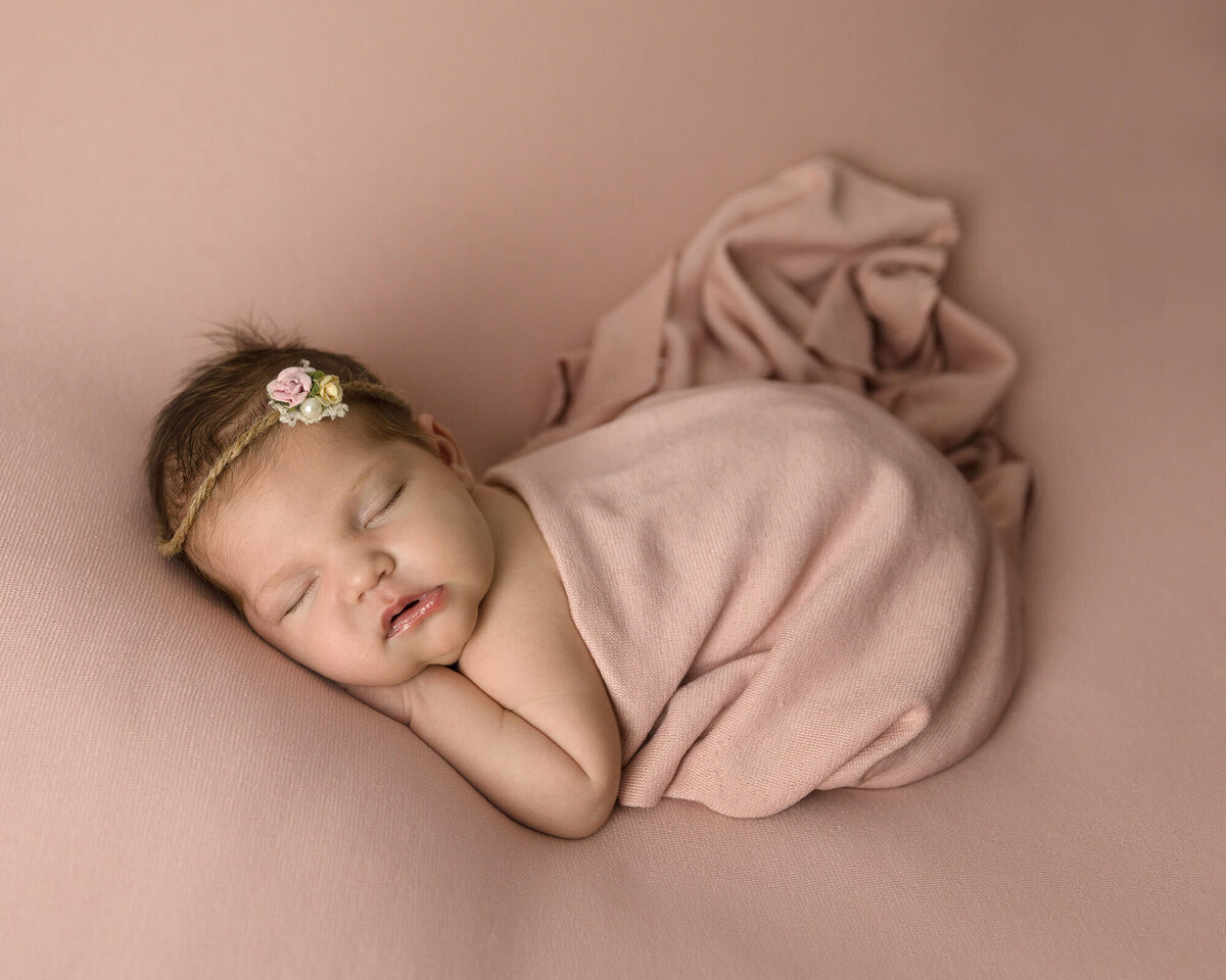 Newborn girl wrapped in a peach wrap laying on her tummy sleeping.