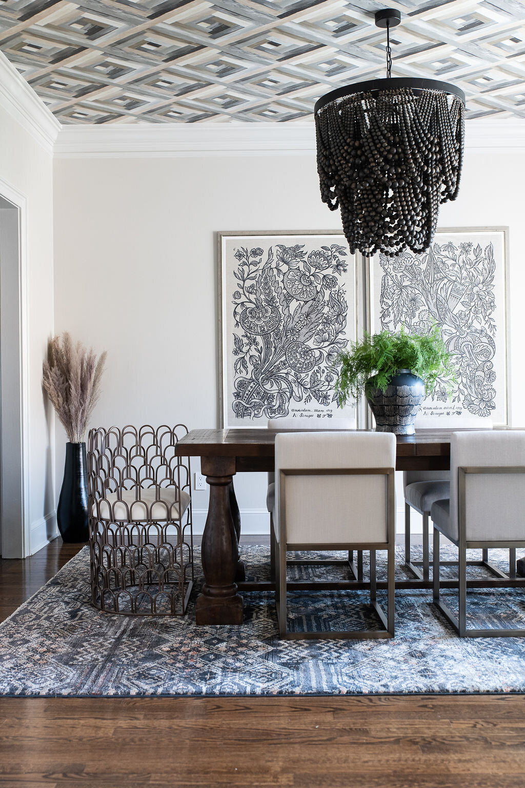 a dining room with a long, wooden dining table, chairs with white cushions, and botanical artwork on the walls