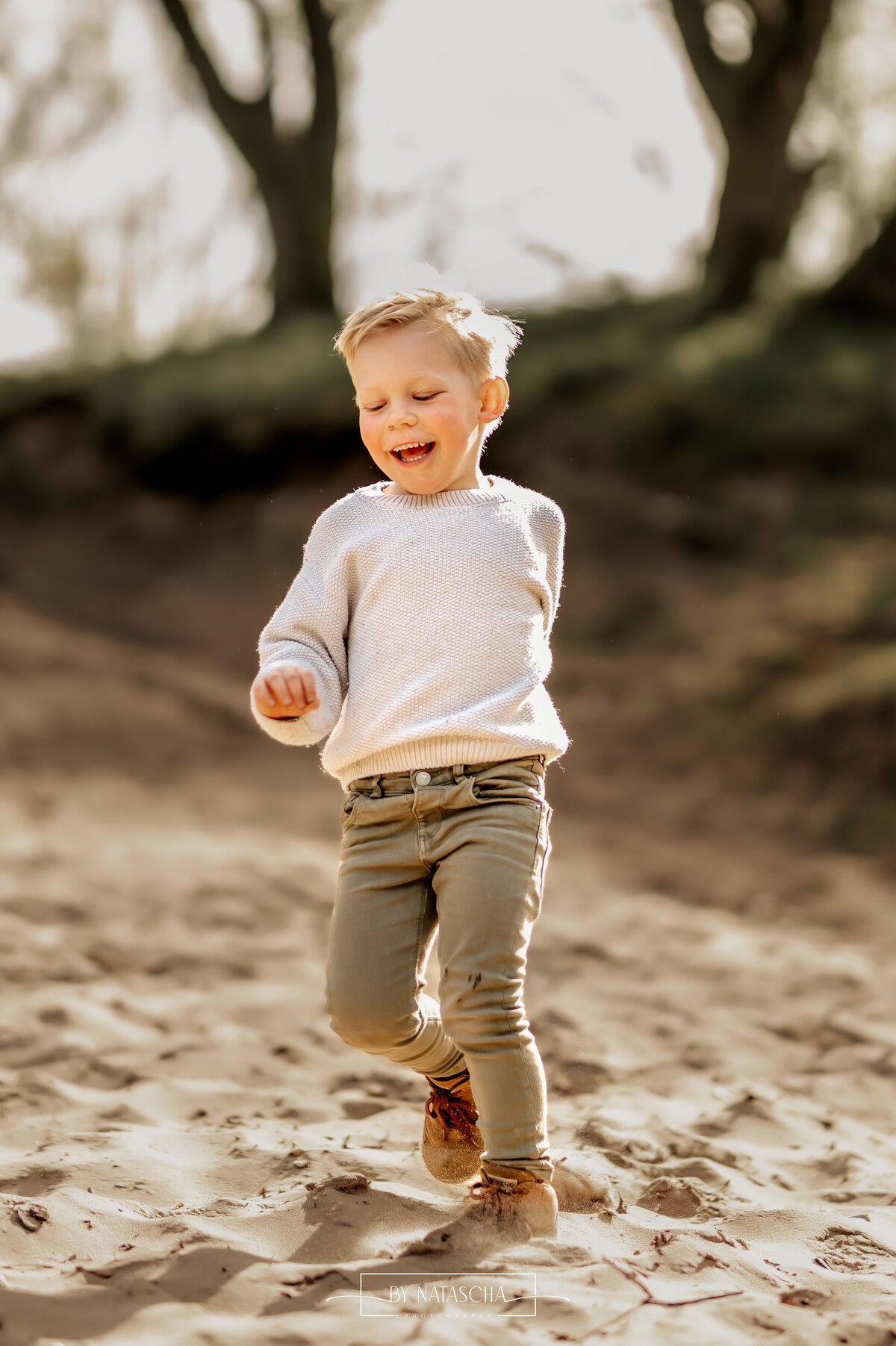 Jongen rent van de duinen af en lacht met de zon die door zijn haren schijnt