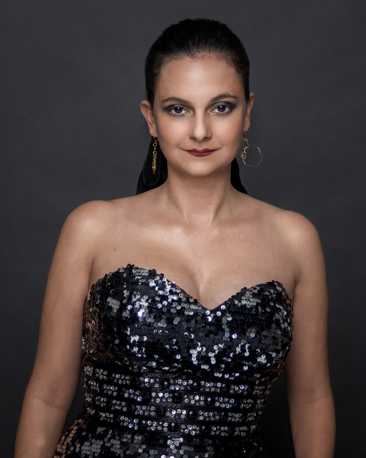 woman in black sequence dress standing forward in front of dark background in studio