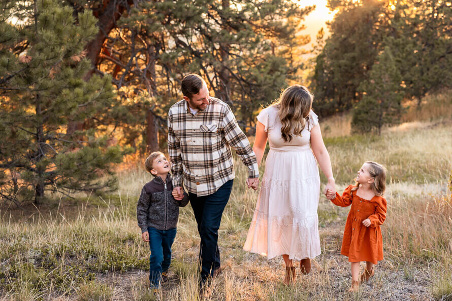 Family holds hands and walks through the evergreens while looking at each other.