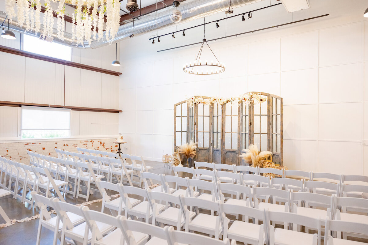 A bright and elegant wedding ceremony space at Maplewood Events in Spanish Fork, Utah. Rows of white chairs face a rustic wooden backdrop adorned with soft pampas grass and floral accents, creating a warm and inviting atmosphere.