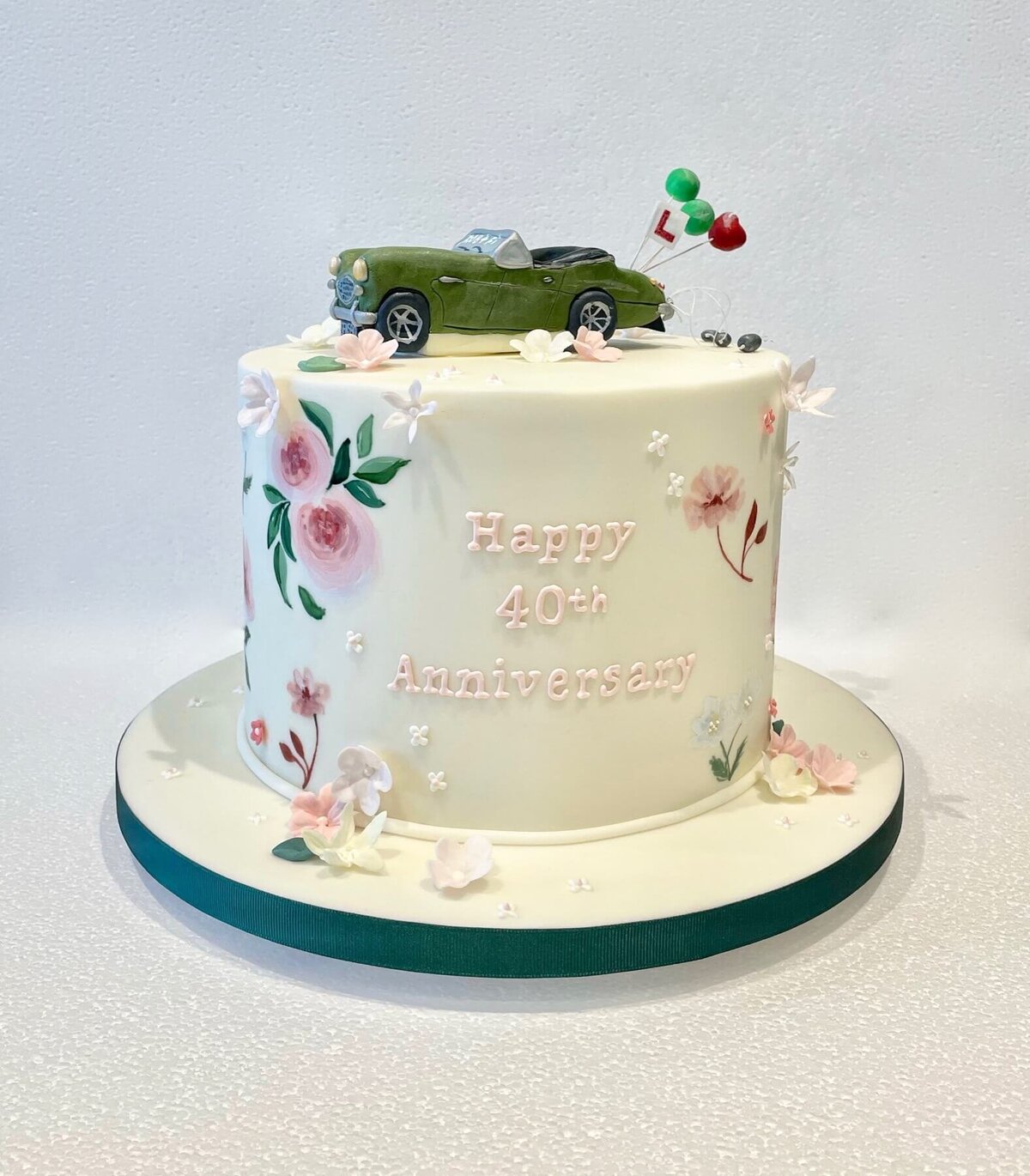 A hand painted birthday cake with delicate sugar flowers and a car on top
