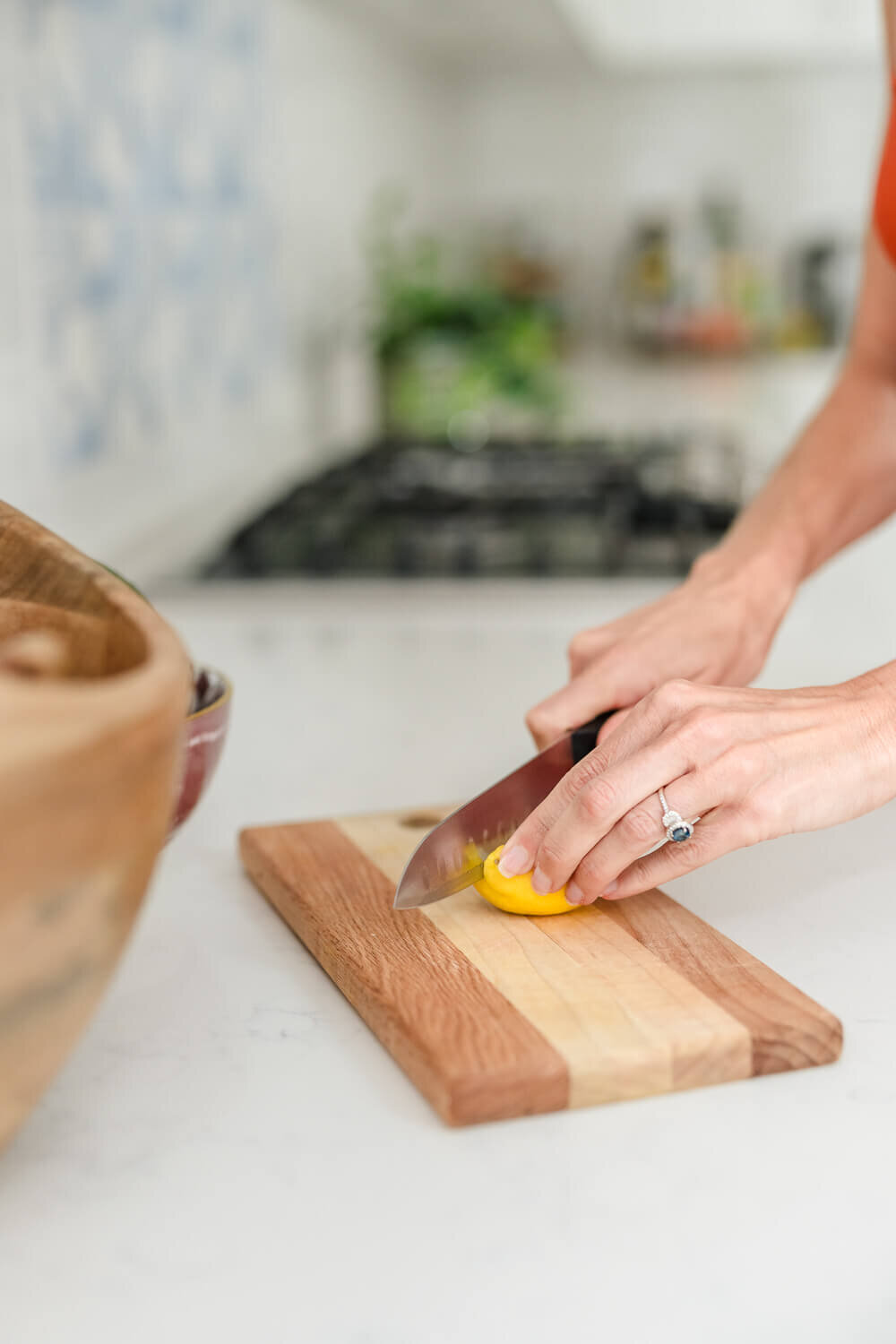 Close-up of woman slicing lemon on striped wood cutting board in bright white kitchen.