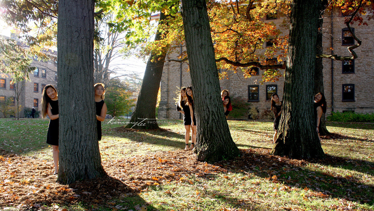 Eight girls hiding behind three autumn trees