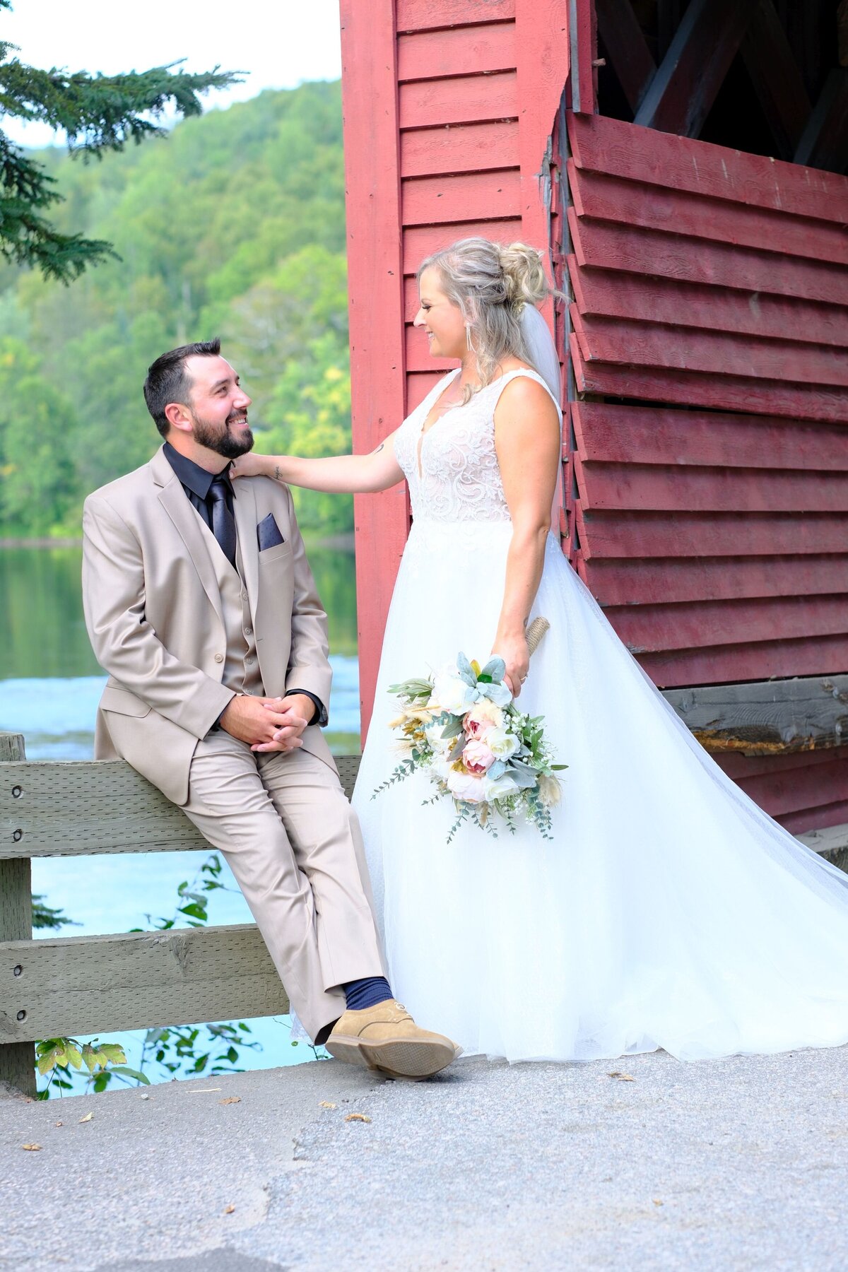 The bride places her hand on the groom's shoulder as they share a joyful smile. This tender moment captures their affectionate connection and mutual happiness.