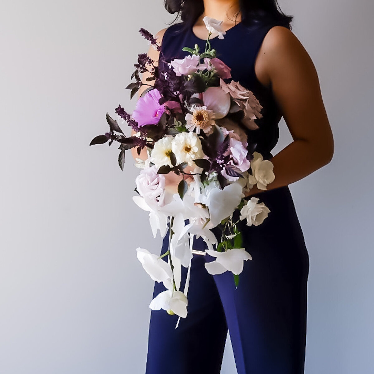 Kathiya in a navy outfit holding a modern bouquet with deep purple roses, orchids, and white flowers.