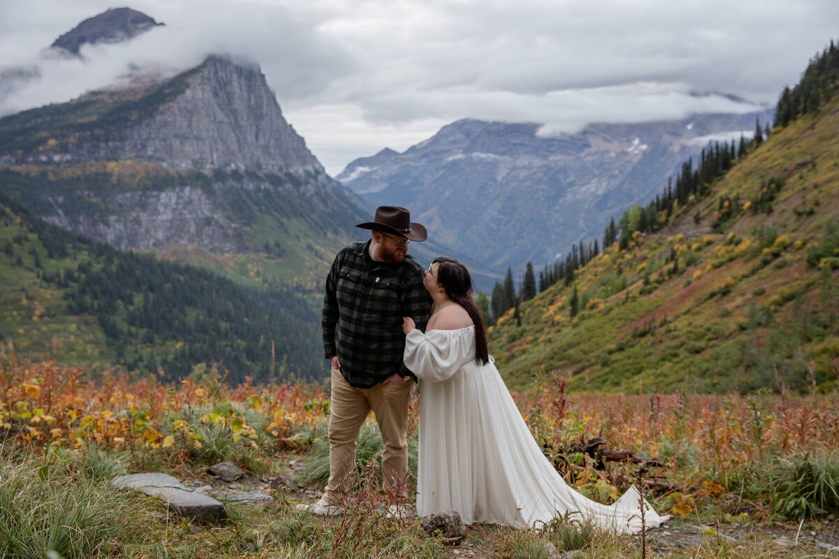 A bride looks up at her groom as she stands holding his arm in Glacier National Park.