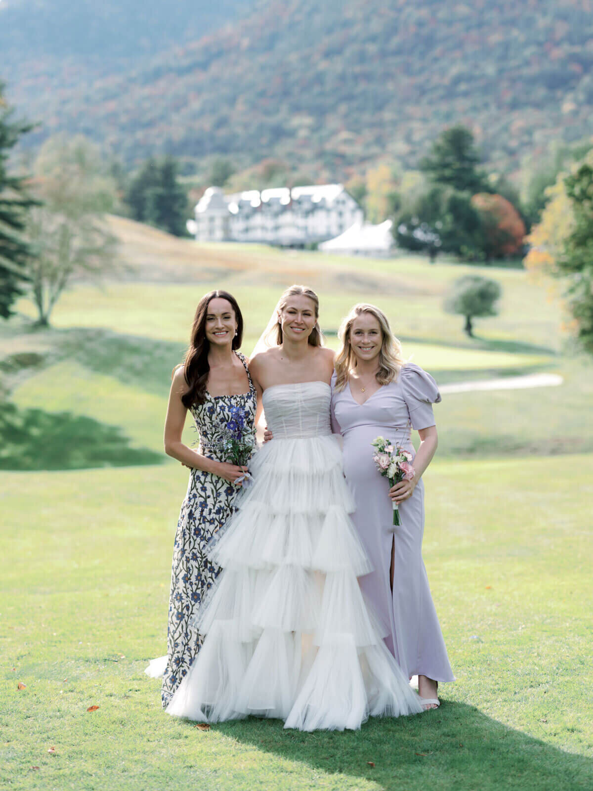The bride with two women at The Ausable Club golf course, hotel and mountains in the background. Image by Jenny Fu Studio.
