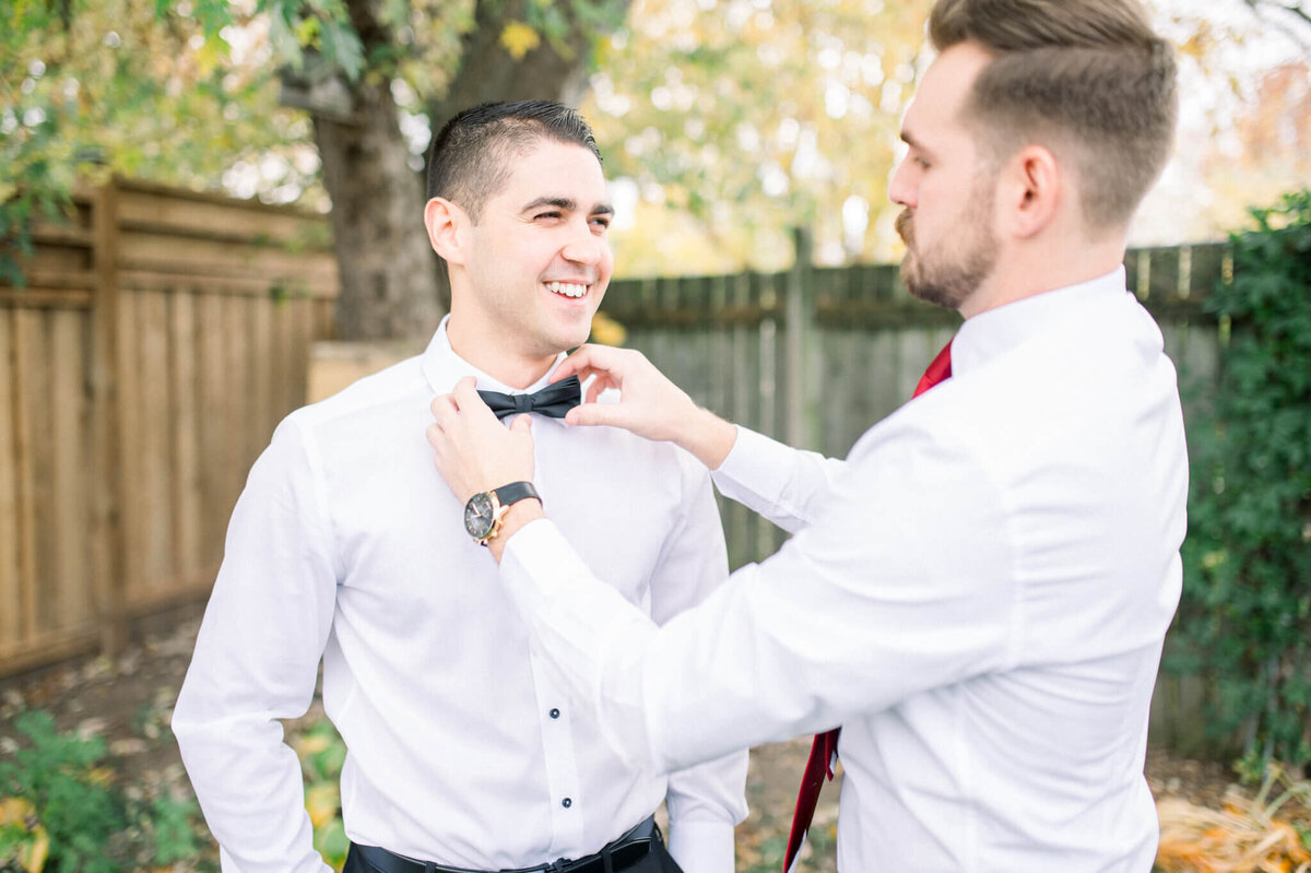 Best man helping groom adjust his bow tie