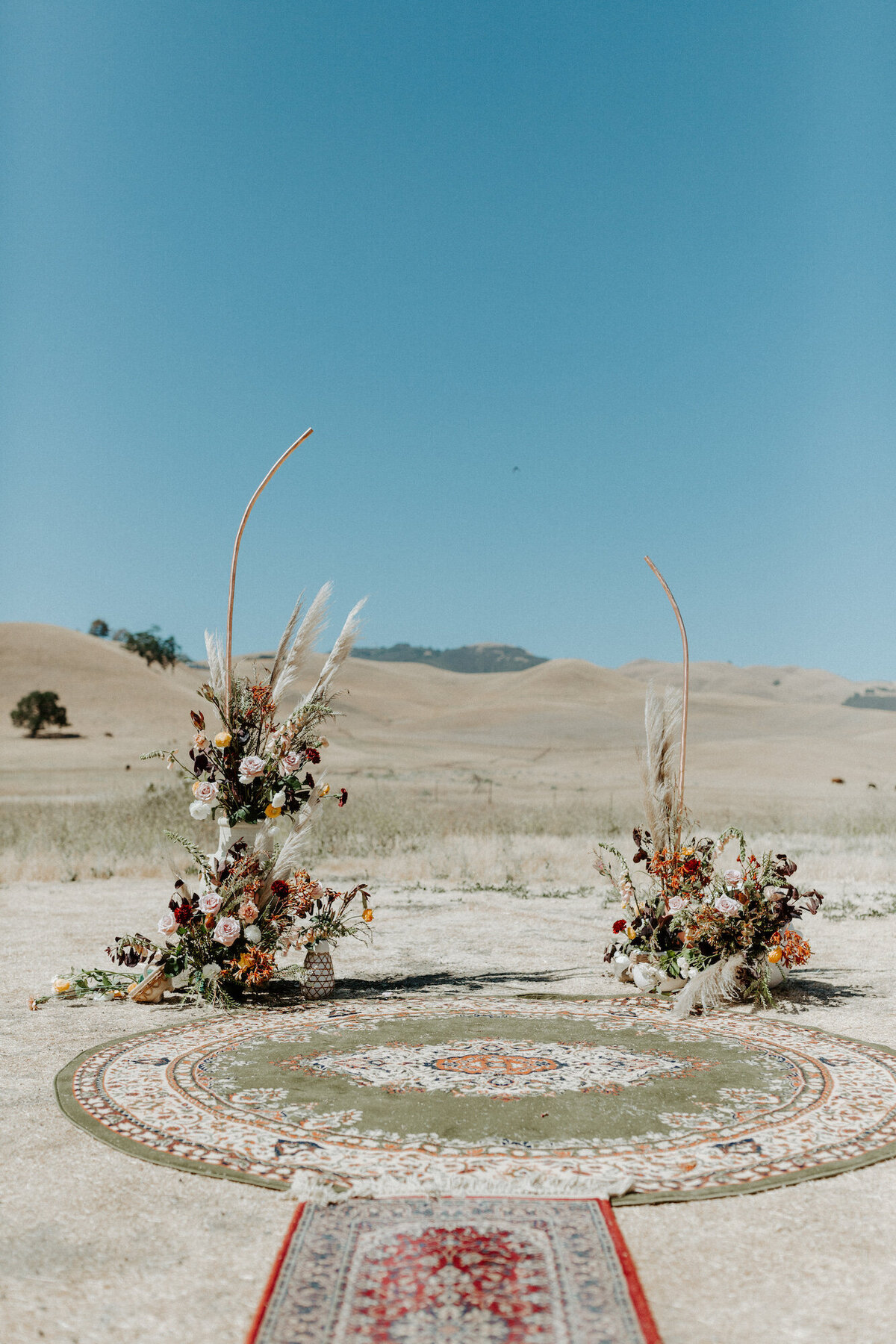 Boho ceremony site with rugs and dried florals and grasses on a ranch