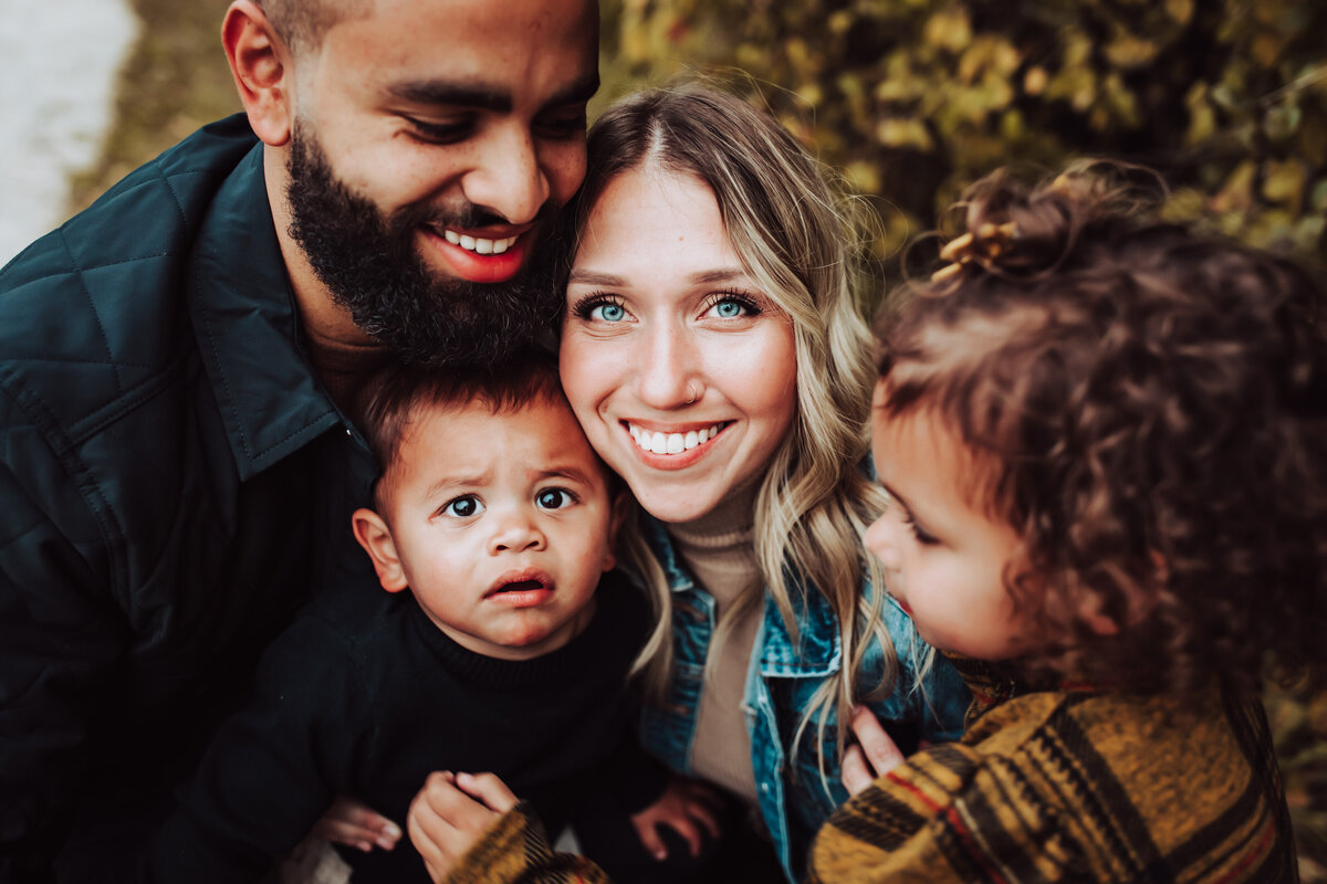family snuggles, smiling at the camera, in Toledo park