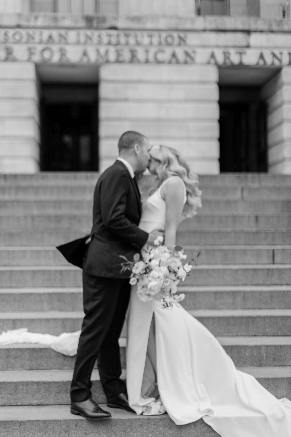 A bride and groom kiss on the stairs of the Smithsonian museum of Art.
