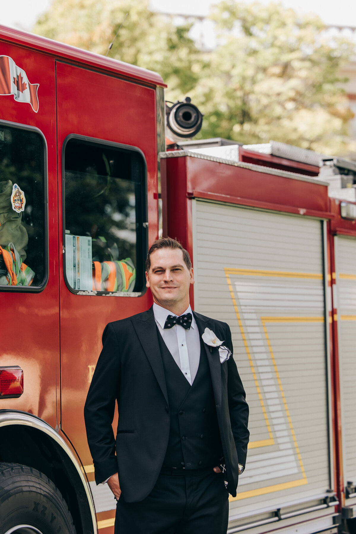 Groom in a black tux posing for portraits with a fire truck