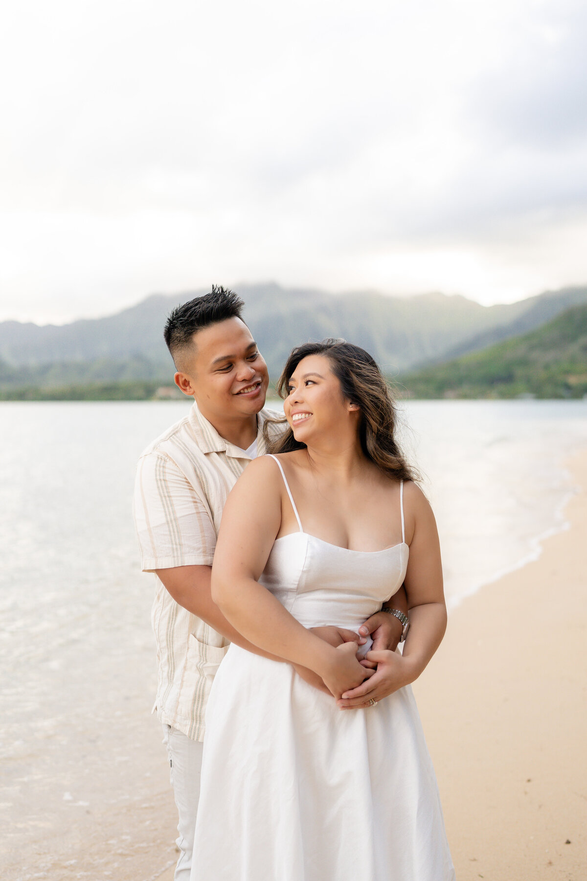 Oahu Hawaii Elopement Asian couple at Secret Island Beach during golden sunset with mountains and ocean waves.