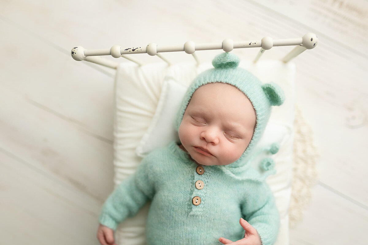 Tiny baby boy asleep on a white metal bed for his newborn photo session.