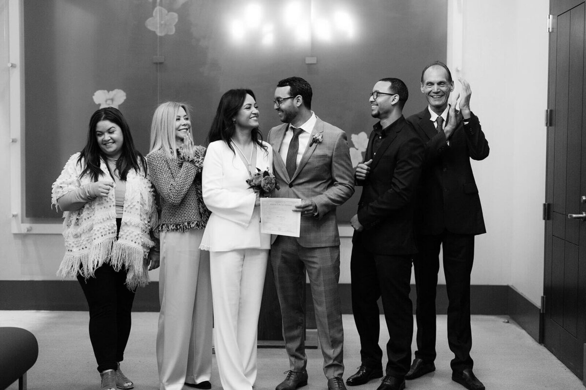 The bride, groom, and four witnesses are all smiling after the ceremony inside New York City Hall. Image by Jenny Fu Studio