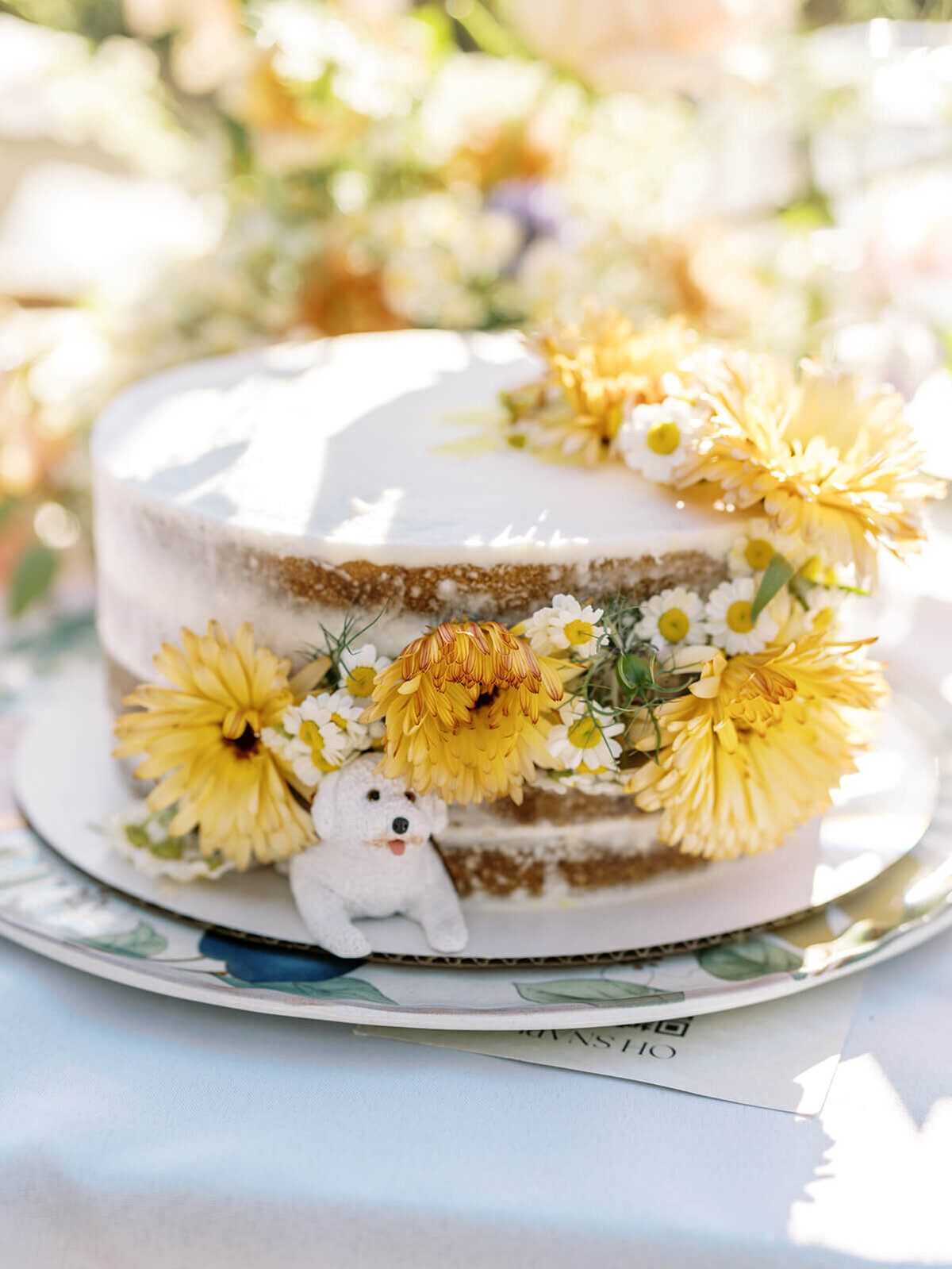 A wedding cake with flowers and a white dog figurine.