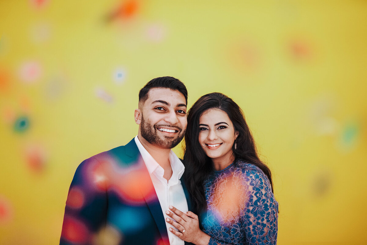 Smiling couple posing together in front of a bright yellow backdrop during a colorful engagement-style photo session in Central Florida.