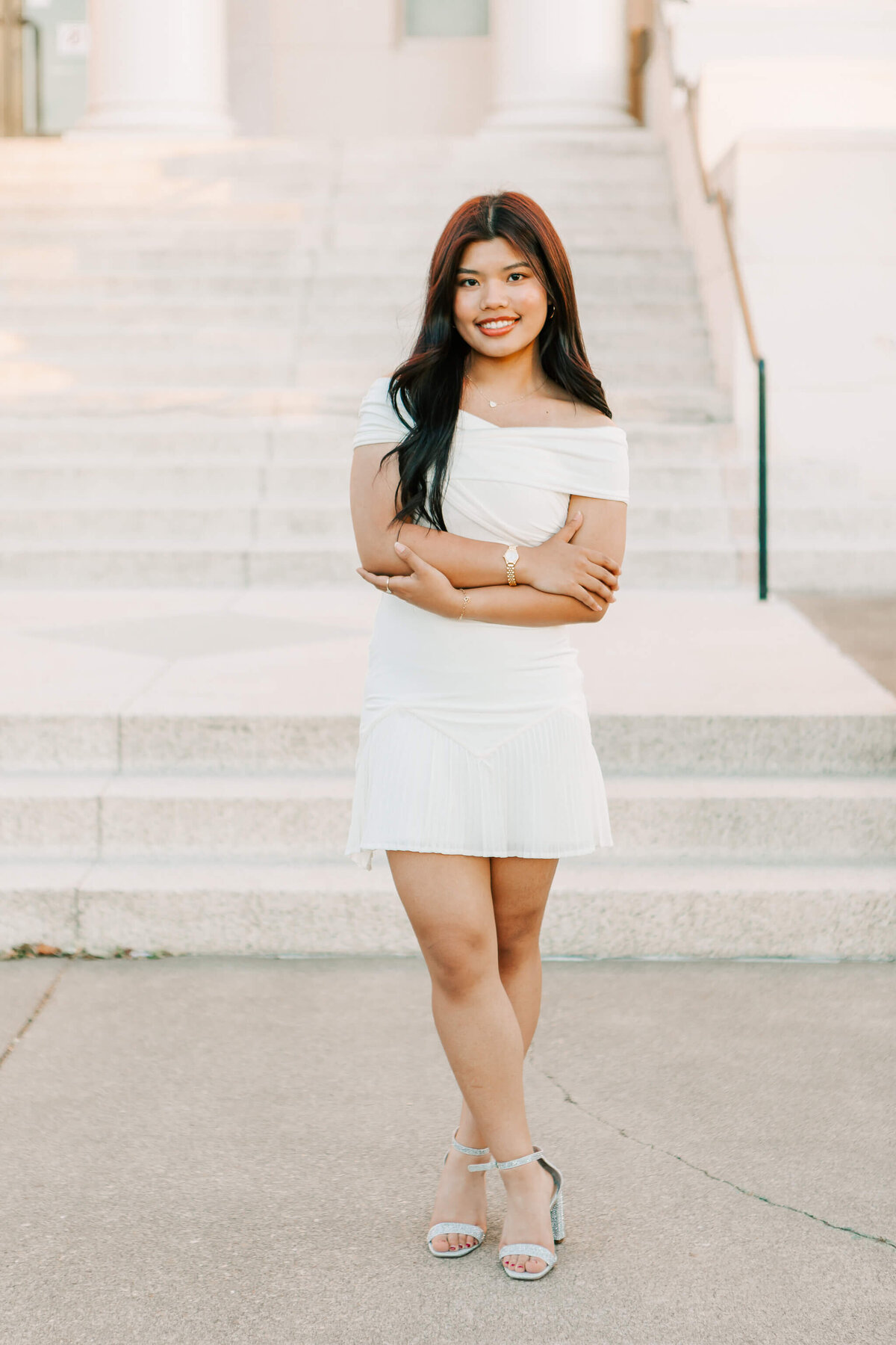 A high school senior stands in a white dress downtown Albany, OR with her arms crossed
