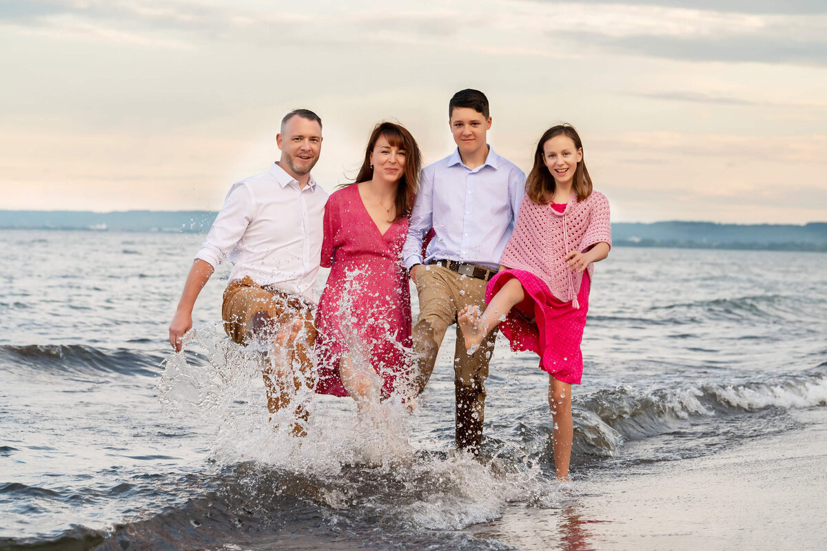 mom and dad with teenage sone and daughter standing in the water splashing with their feet for their Burlington, On beach family photography session