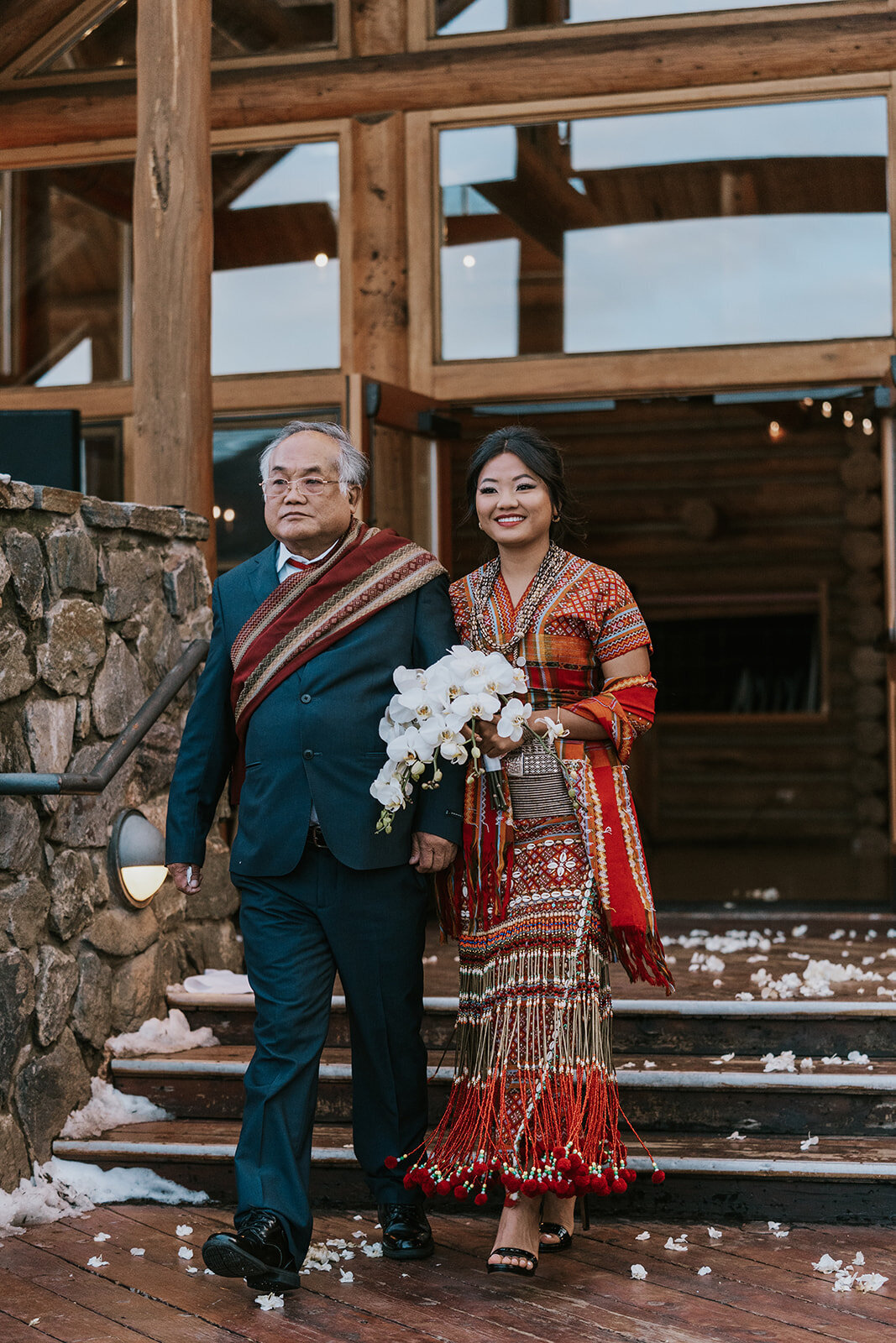 Bride walks down the aisle with her father holding a white orchid bouquet.