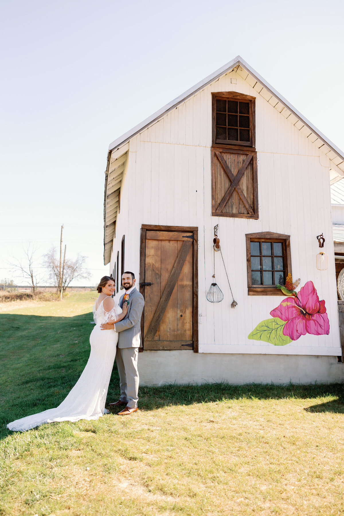 Couple standing outside white barn with rustic wood doors at The Hummingbird Chateau.