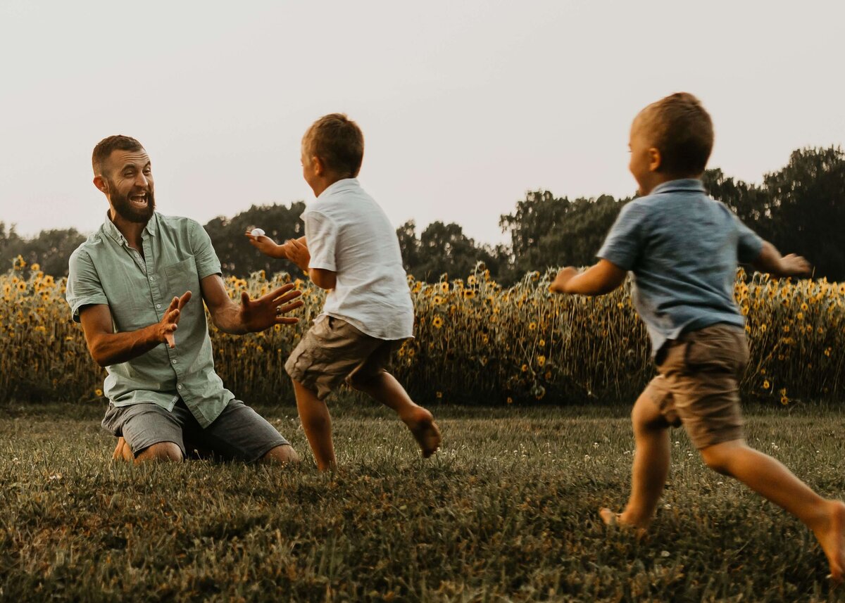 A man playing with his two sons in a field, captured by a Pittsburgh family photographer.