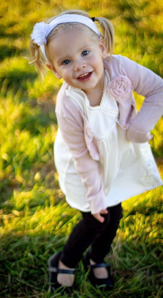 a little girl in a white dress with a pink cardigan playing in a field