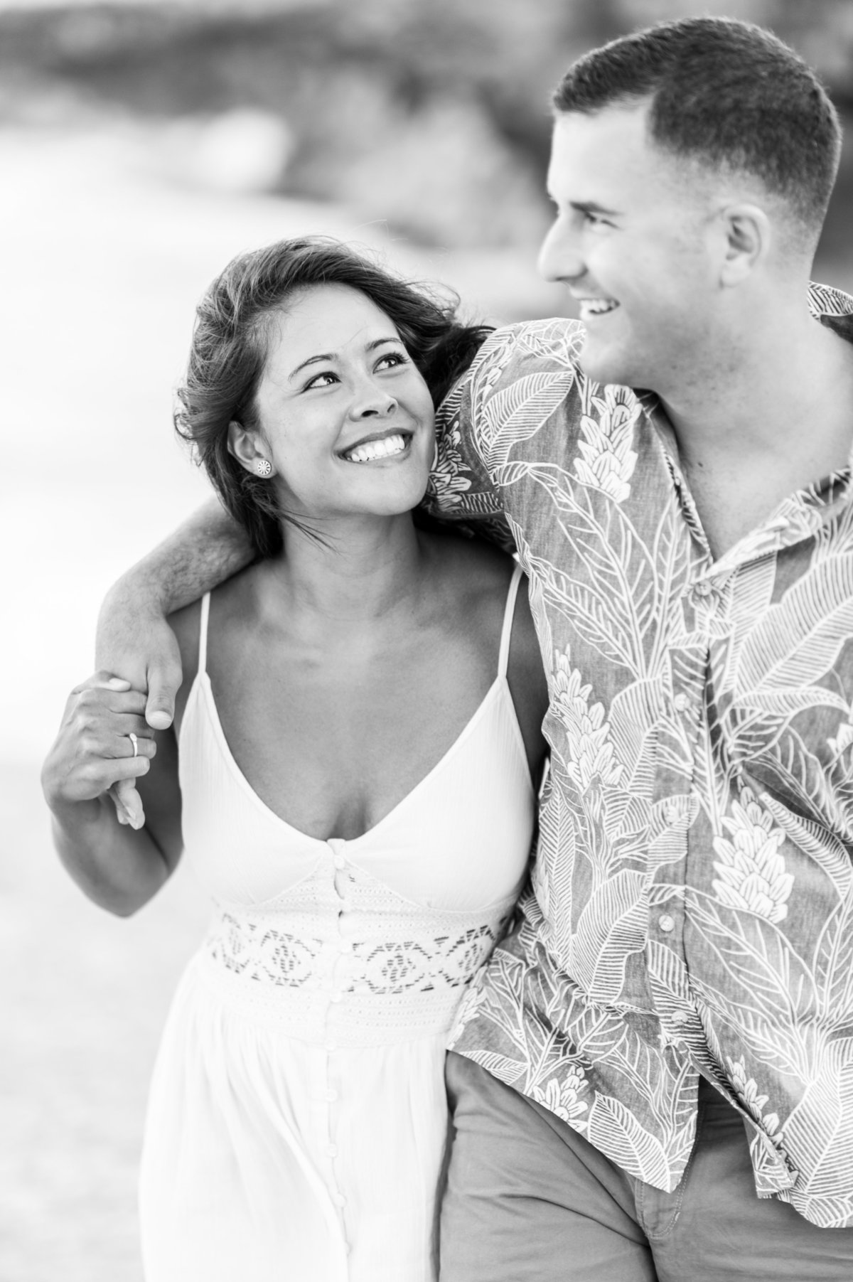 Young couple smiling as they walk arm in arm on the beach.