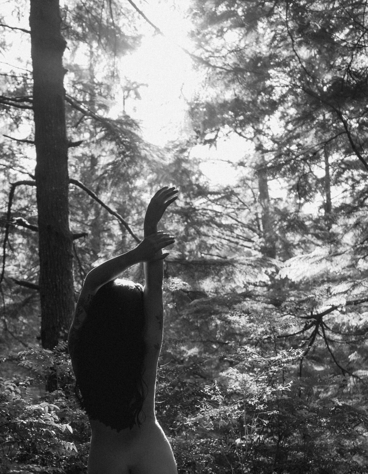 woman poses and stretches out her arm while standing in lush Oregon forest