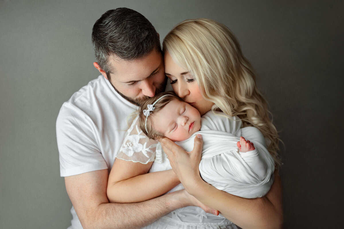mom, dad, toddler son, and newborn baby boy in a white swaddle looking at eachother laughing at a newborn photography session with a photographer in a tysons corner va photo studio