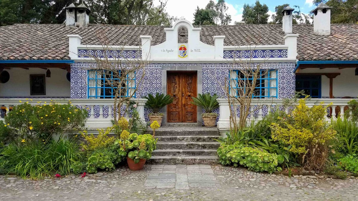 Historic hacienda with blue and white tilework, wooden doors, and lush gardens in the Otavalo Valley, Ecuador ©Stephanie Dosch | theViatrix Luxury Travel