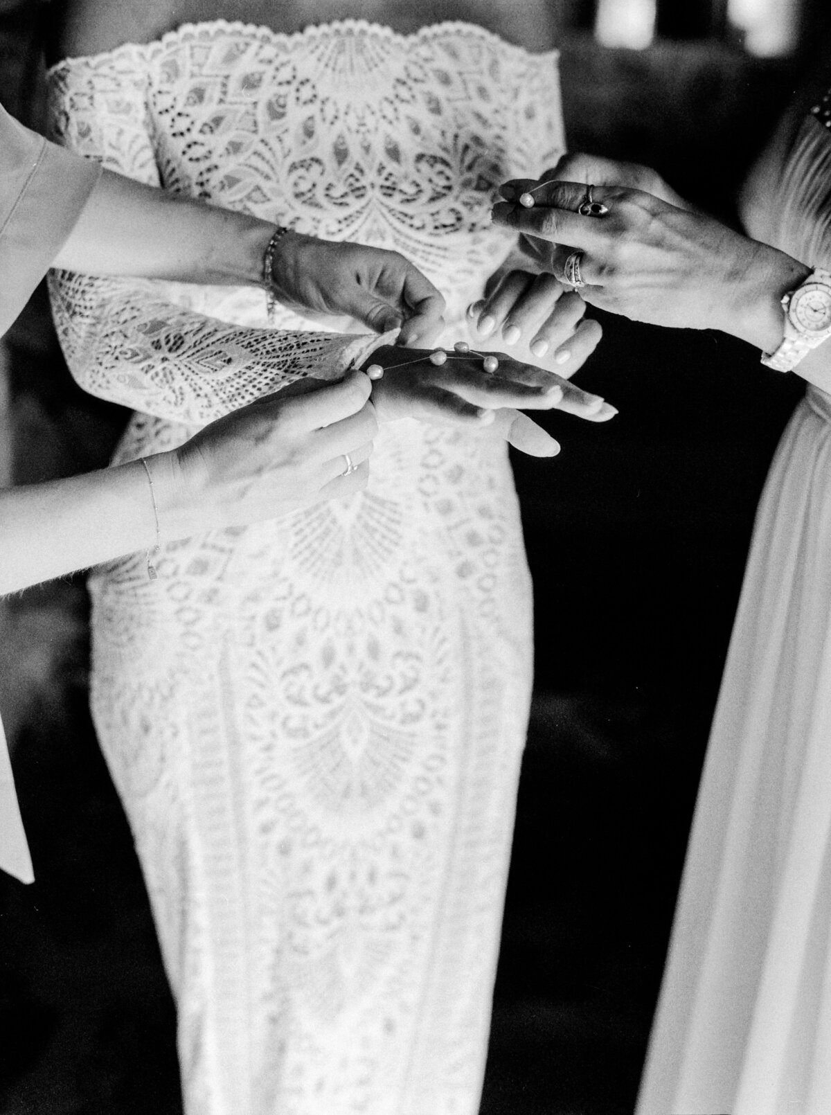 Black and white film photograph of bride in all lace wedding dress while being helped by maid of honor and mother photographed by Italy wedding photographer at Villa Montanare Tuscany wedding