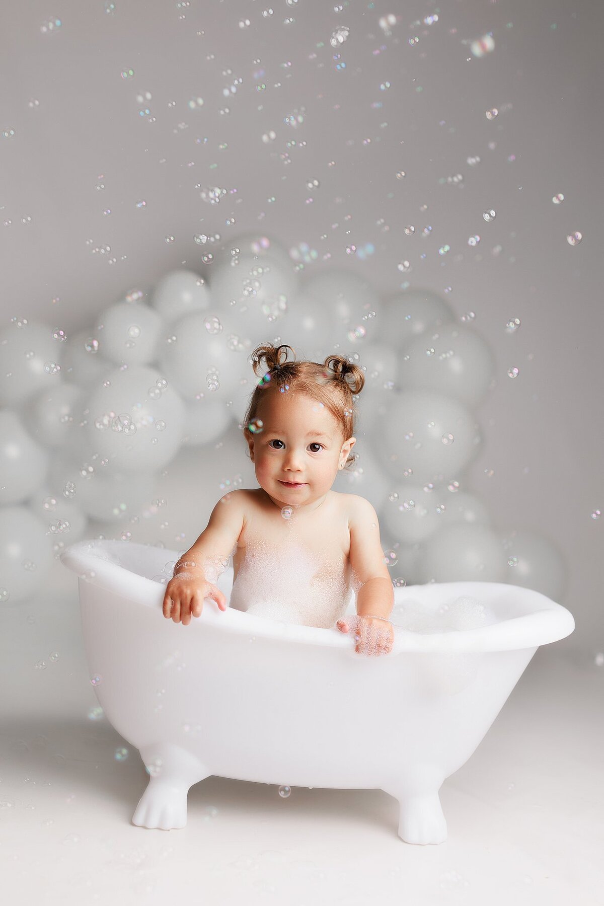 Smiling baby sitting in vintage tub during milestone bubble bath session