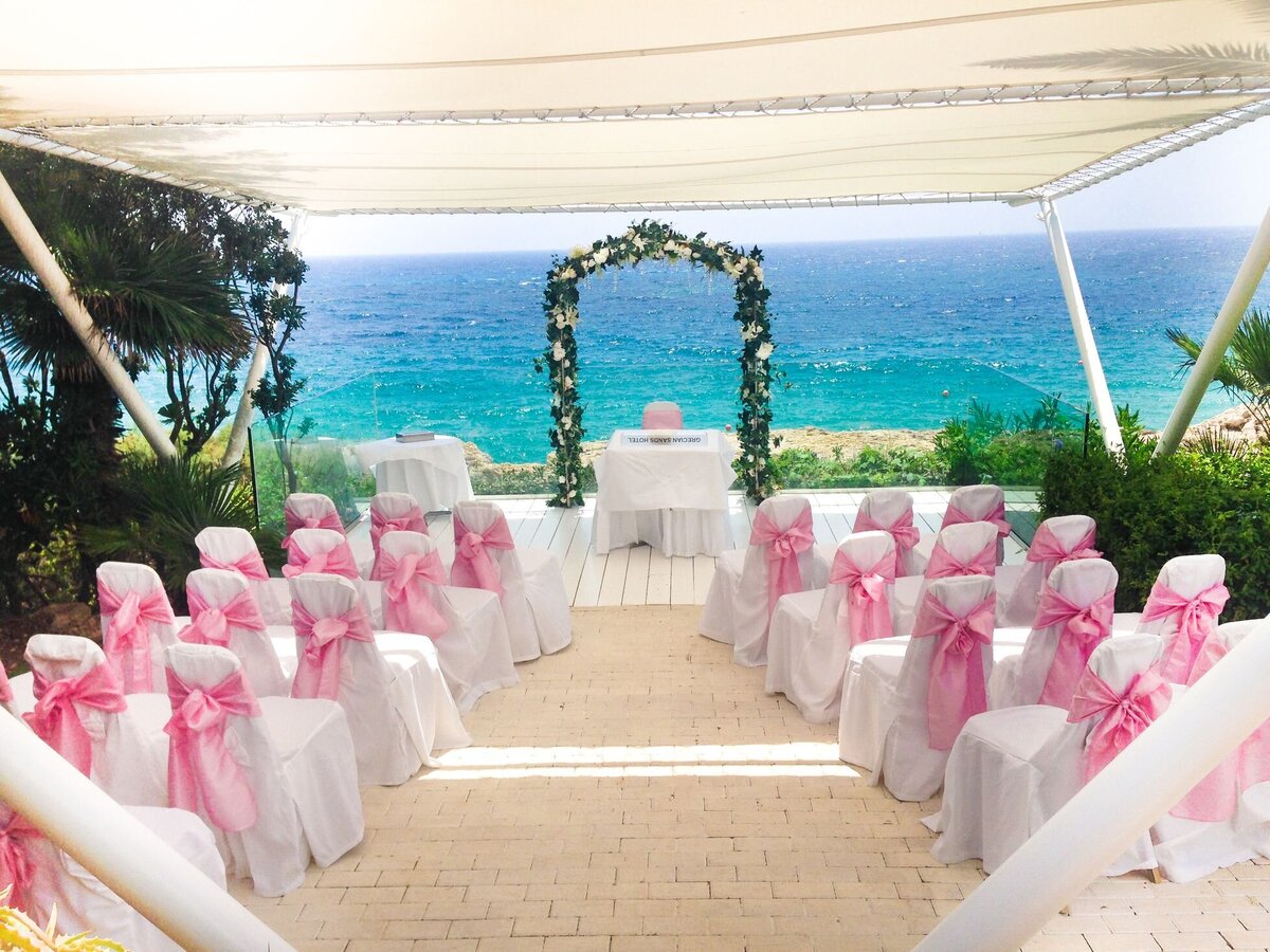 White chairs adorned with pink sashes make a beautiful contrast to the beautiful blue sea in the background