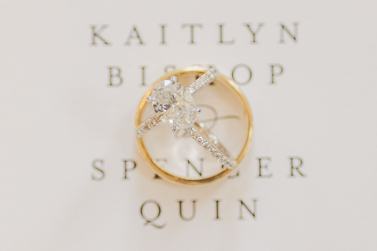 Close-up of classic gold and diamond wedding rings styled on wedding invitation, photographed at a romantic Denton, Texas wedding.