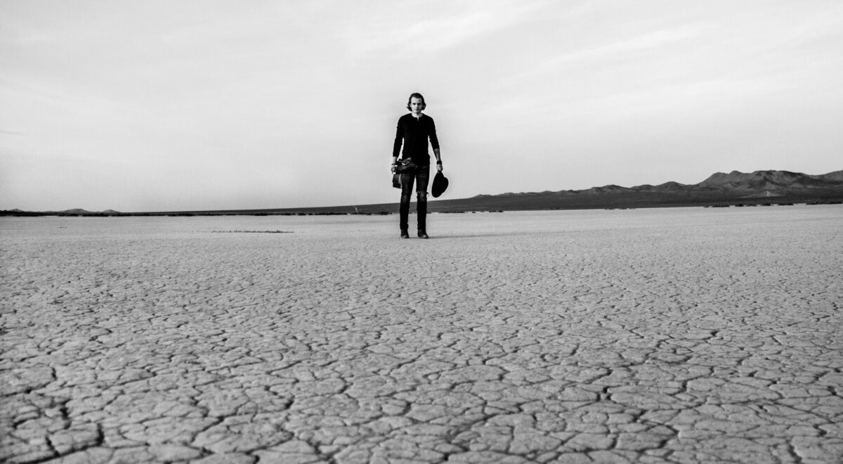 Black and White musician portrait Cole Bradley standing in long shot cracked desert floor in foreground El Mirage