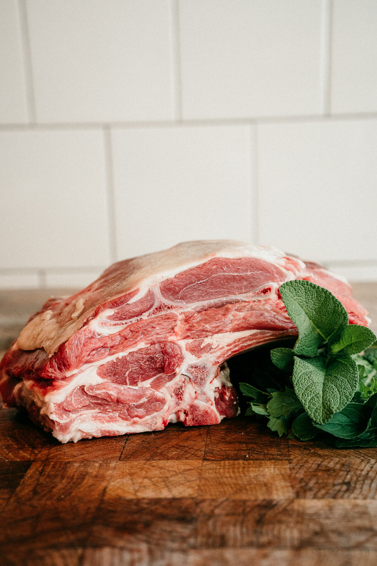 cut of meat against white subway tile with green herbs