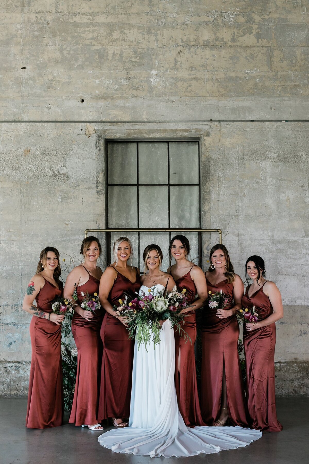 Bride and bridesmaids smiling for their portraits in the chapel at Olde Dobbin Station. The bridesmaids are in burgundy dresses from Revelry.