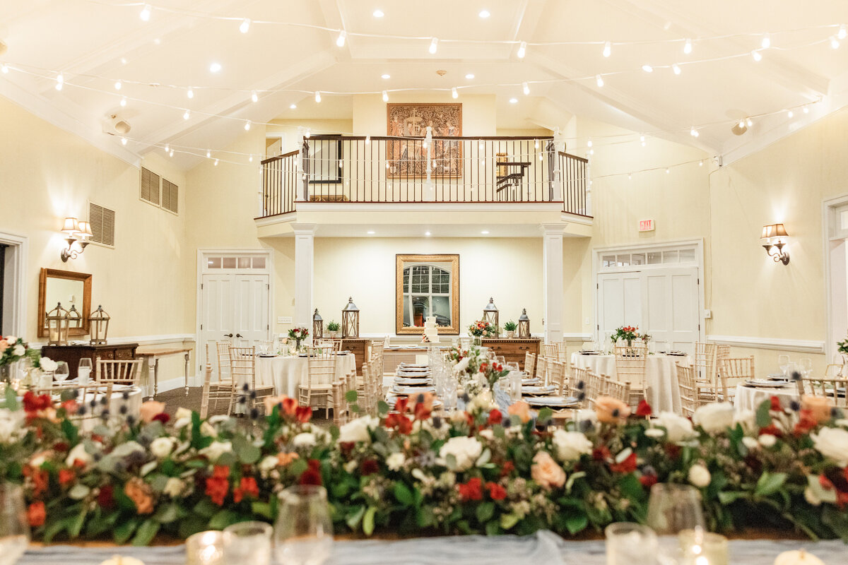 A wedding reception hall with floral arrangements laid out on rectangular tables