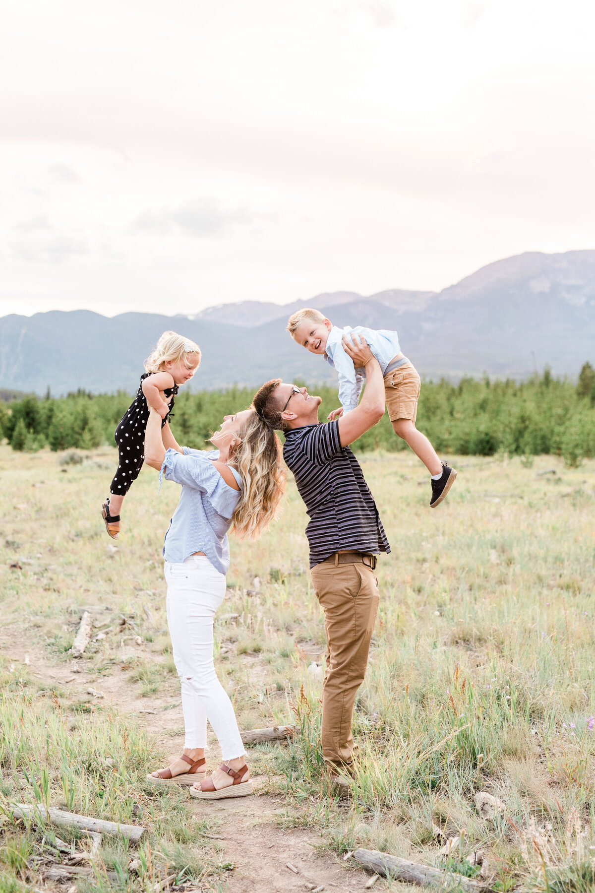 Two parents stand back to back as they swing their young children joyfully above their heads
