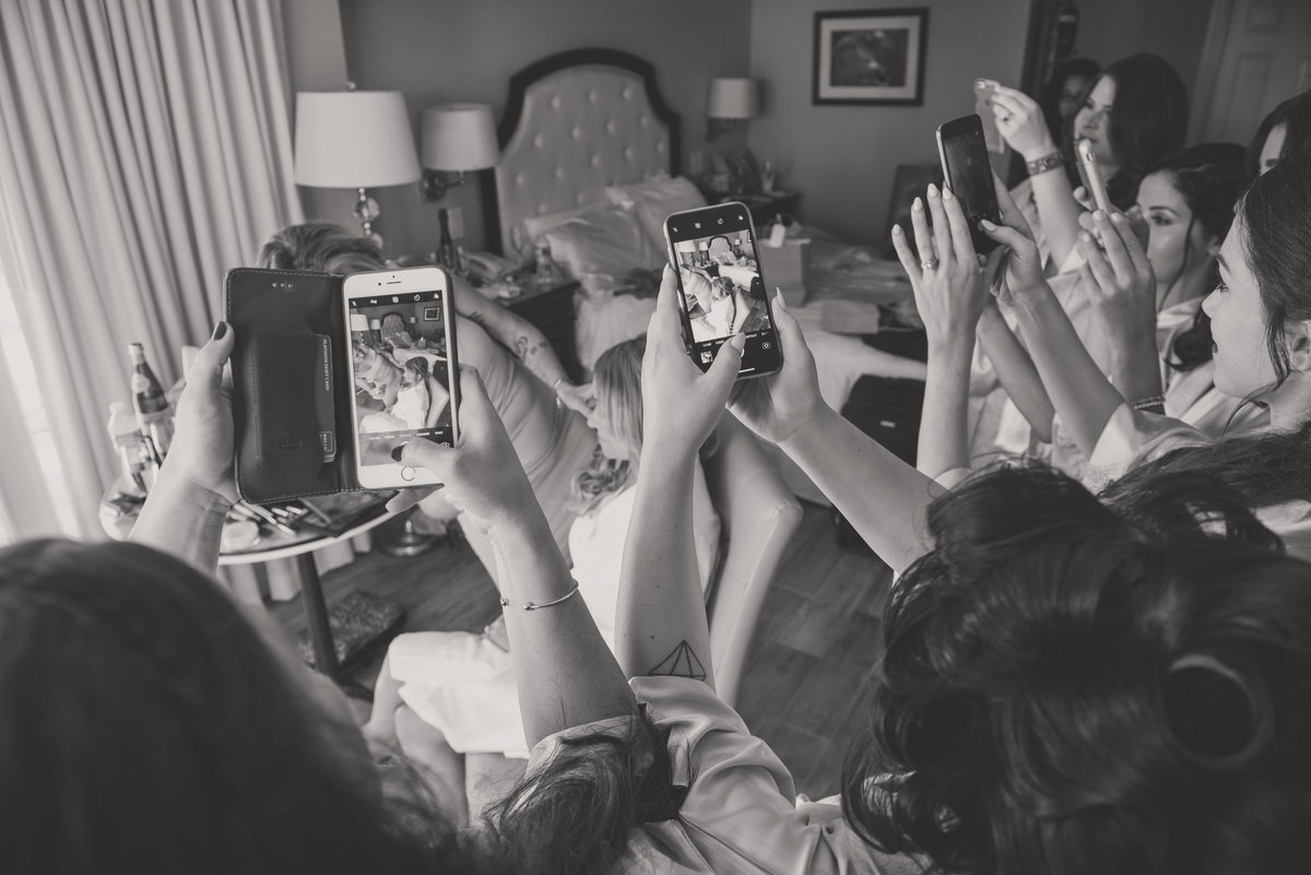 Bridesmaids holding cellphone to take a photo of a bride