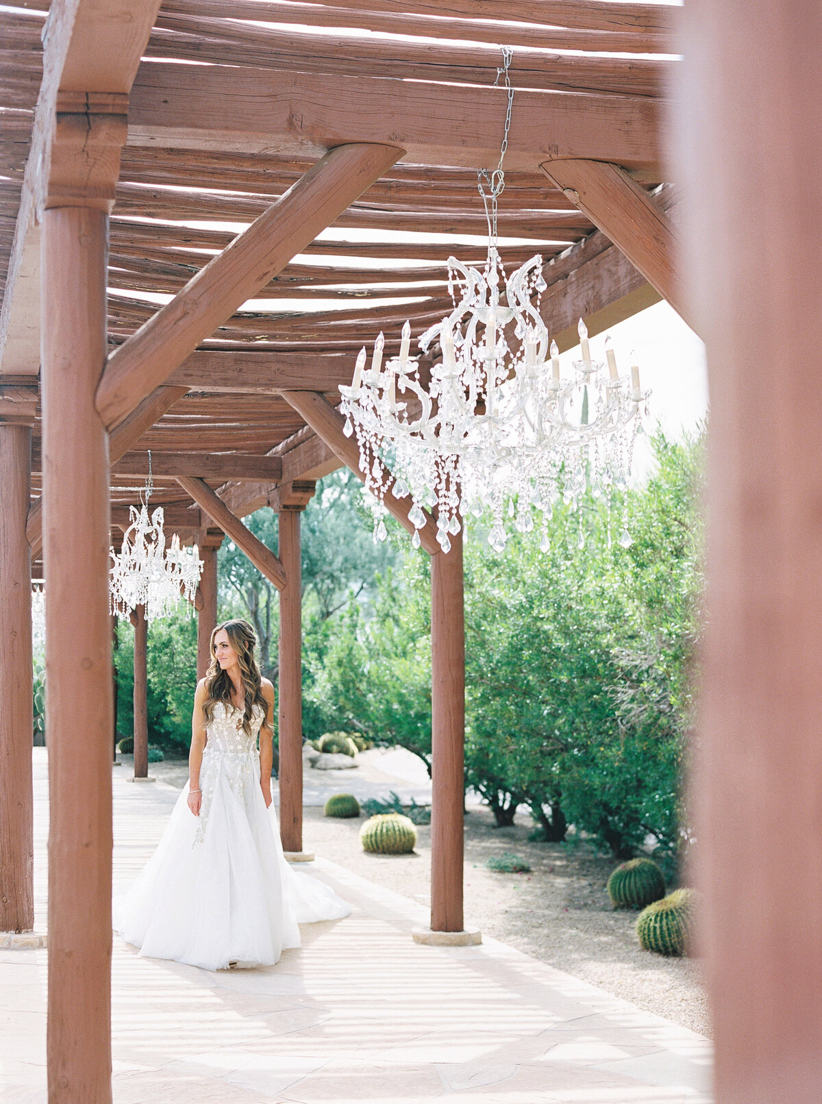 The bride gracefully walks beneath elegant crystal chandeliers in a romantic desert wedding venue, blending rustic charm with luxury decor.